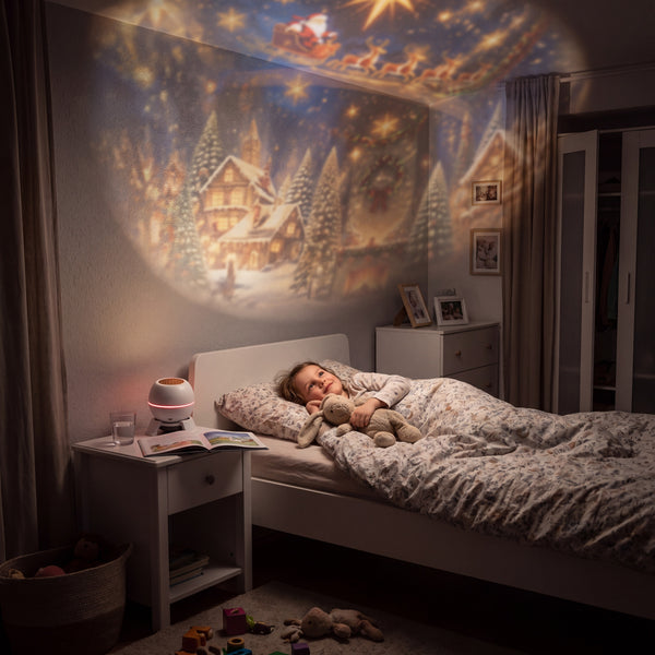 Girl in bed looking up at a soft Christmas scene projected on her bedroom wall and ceiling