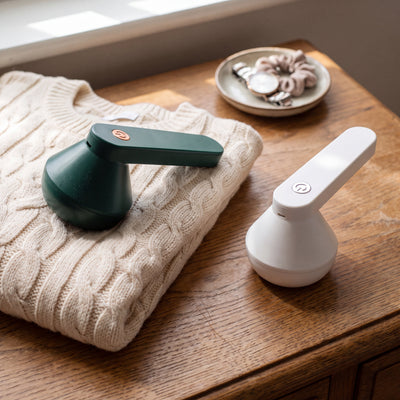 Novum Electric Lint Remover in Green and White on a dresser with a cream sweater