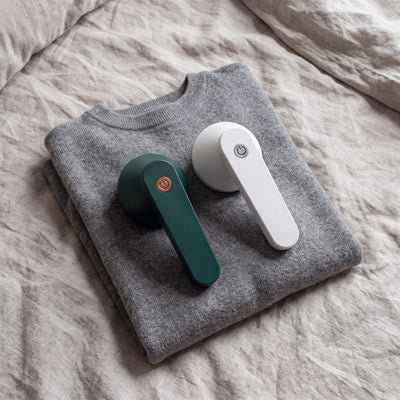 Green and White Novum Electric Lint Removers on a folded grey sweater