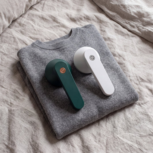 Green and White Novum Electric Lint Removers on a folded grey sweater