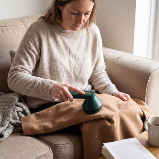Woman holding the green Novum Electric Lint Remover on a camel coat