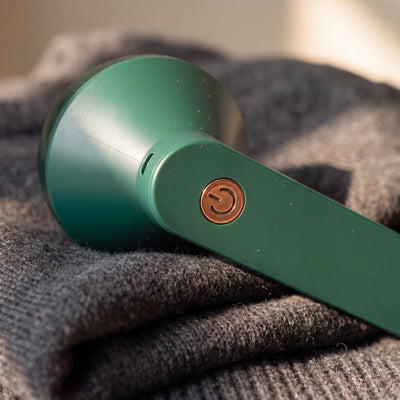 Copper-coloured power button on the green Novum Electric Lint Remover