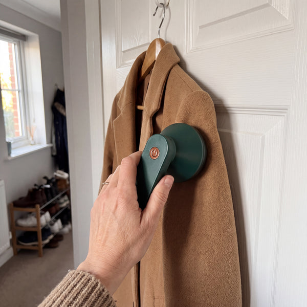 Green electric lint remover held against a camel wool coat