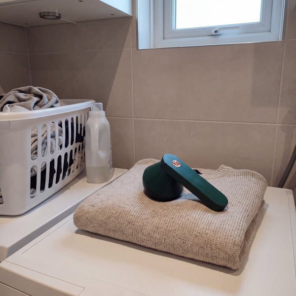 Green electric lint remover on a folded jumper in a laundry room