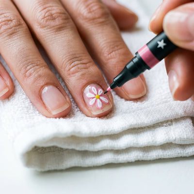 Drawing a small daisy on a fingernail with the fine liner tip of a Novum nail art pen
