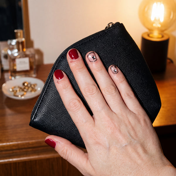 Red nails and two nails with hand-drawn black outlines and stars, hand holding a black clutch