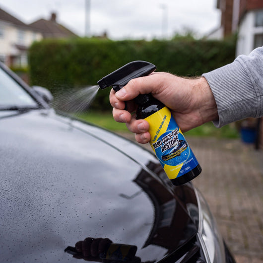 A hand spraying Novum Car Nano Coat Spray onto the hood of a black car