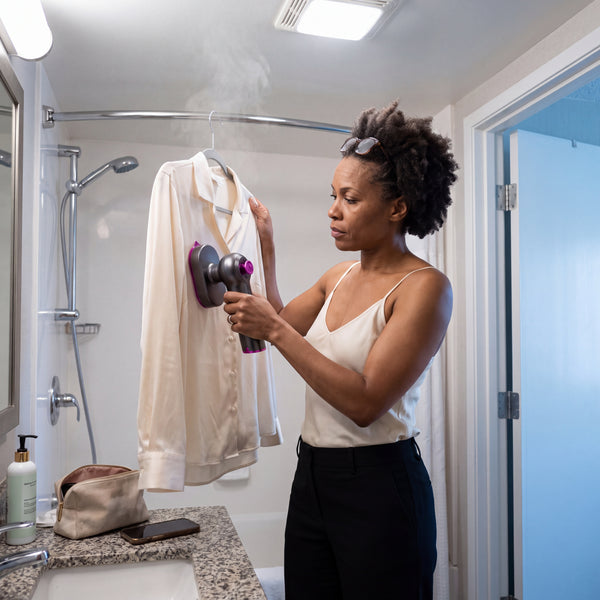 A woman steaming a blouse on a hotel shower rail before work