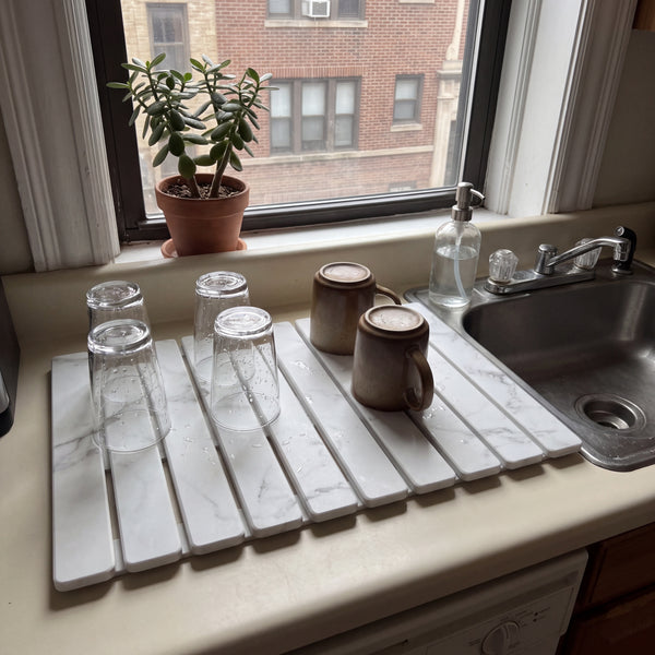Stone dish drying mat by an apartment kitchen sink with glasses and mugs drying