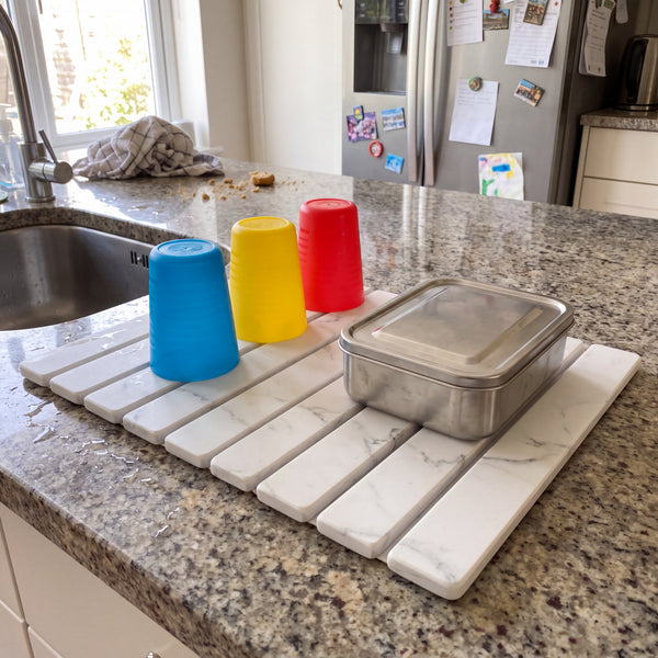 Stone dish drying mat on a granite counter with tumblers and a lunch box