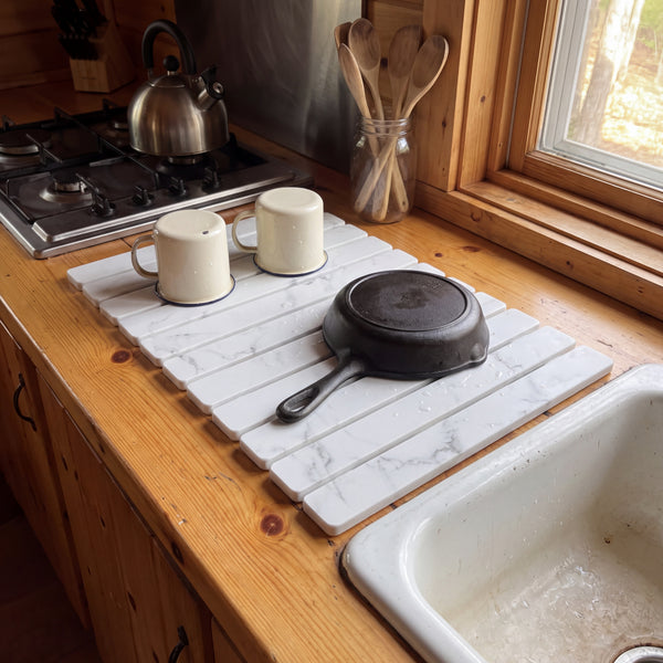 Stone dish drying mat on a pine counter with enamel mugs and a skillet