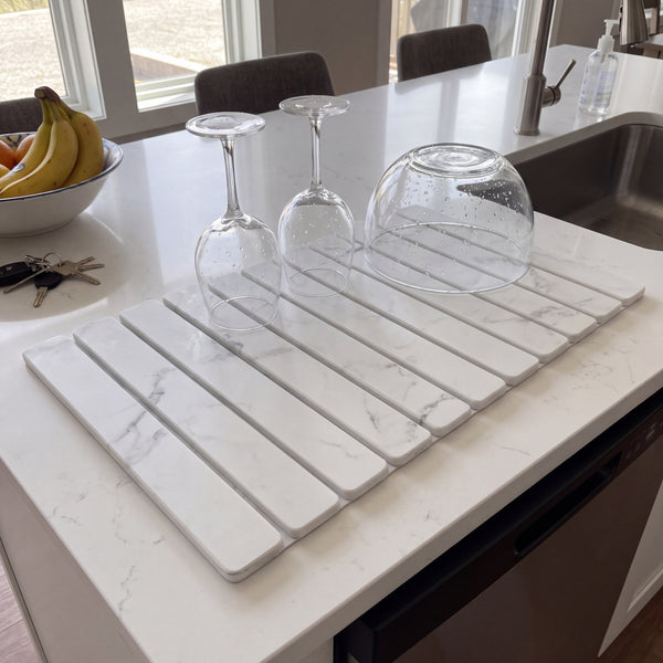 Stone dish drying mat on a kitchen island with wine glasses and a glass bowl