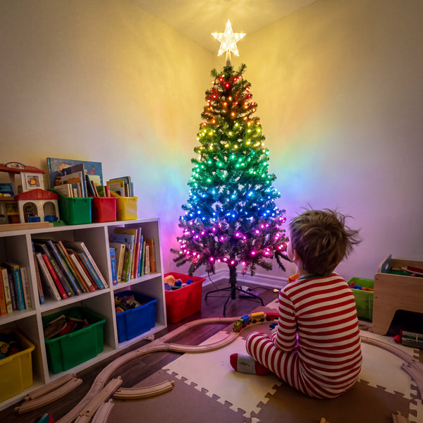 A child in pyjamas looking up at a Christmas tree with multicolour lights