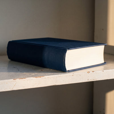 The thick navy hardcover lying on a shelf, showing the rounded spine and the cream page block
