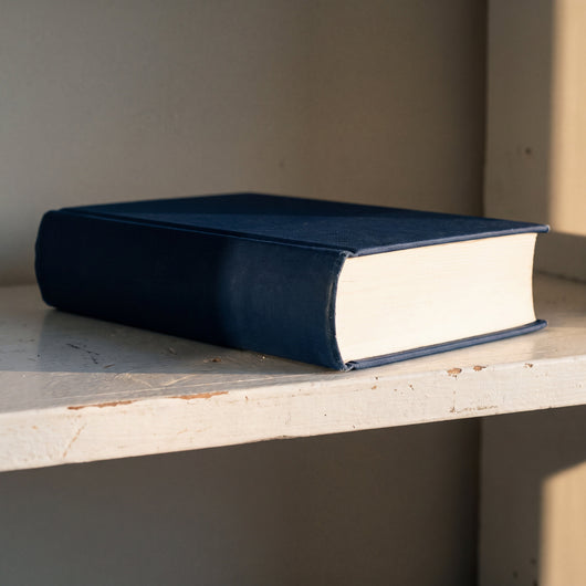 The thick navy hardcover lying on a shelf, showing the rounded spine and the cream page block